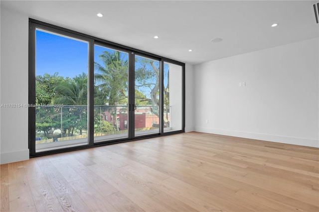 spare room with light wood finished floors, visible vents, baseboards, floor to ceiling windows, and recessed lighting