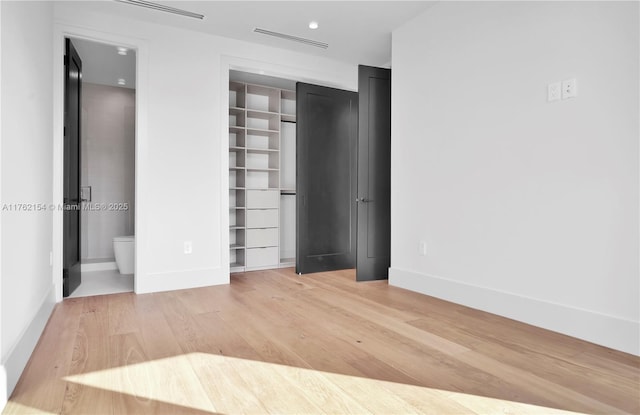 unfurnished bedroom featuring visible vents, light wood-style flooring, ensuite bathroom, a closet, and baseboards