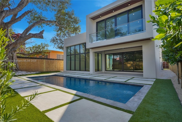 rear view of property featuring stucco siding, a patio, a fenced in pool, and fence