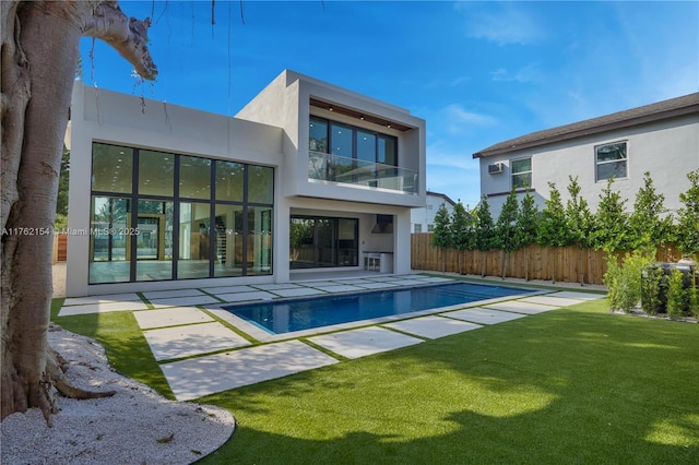 rear view of property featuring stucco siding, a lawn, fence, a balcony, and a patio area