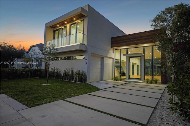 view of front of property featuring stairway, a front yard, stucco siding, a garage, and a balcony