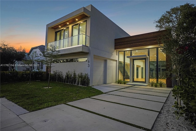 view of front of home featuring a balcony, an attached garage, stucco siding, concrete driveway, and a lawn