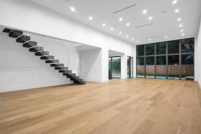 unfurnished living room featuring light wood finished floors, visible vents, stairs, and a towering ceiling