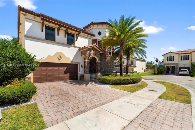 mediterranean / spanish-style house with a tiled roof, stucco siding, decorative driveway, a garage, and stone siding