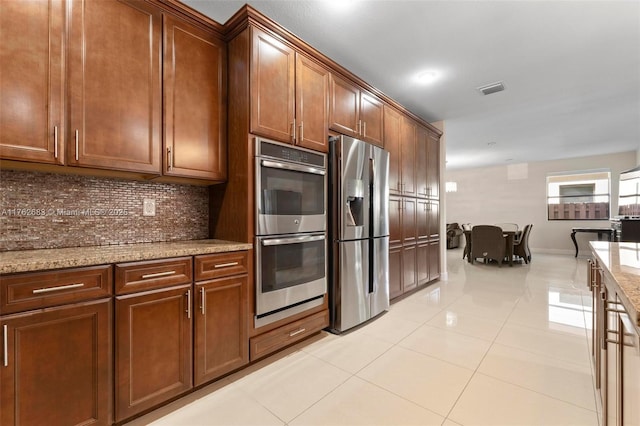 kitchen featuring visible vents, backsplash, light tile patterned floors, light stone counters, and appliances with stainless steel finishes