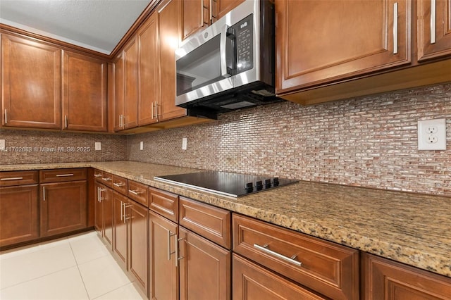 kitchen featuring stainless steel microwave, brown cabinetry, black electric stovetop, decorative backsplash, and light tile patterned flooring