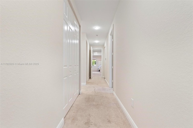 hallway featuring light colored carpet and baseboards