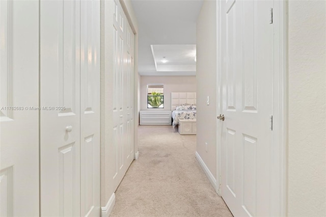 corridor with a tray ceiling, baseboards, and light colored carpet