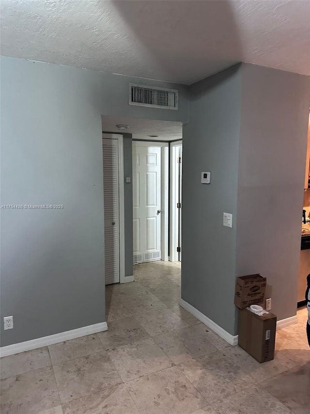 hall with visible vents, baseboards, and a textured ceiling