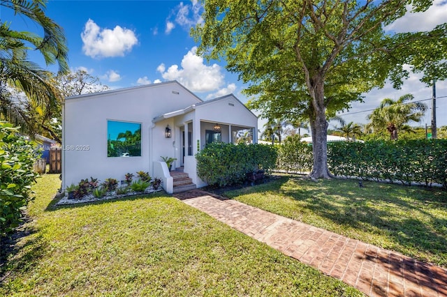 view of front of property with stucco siding, a front lawn, and fence