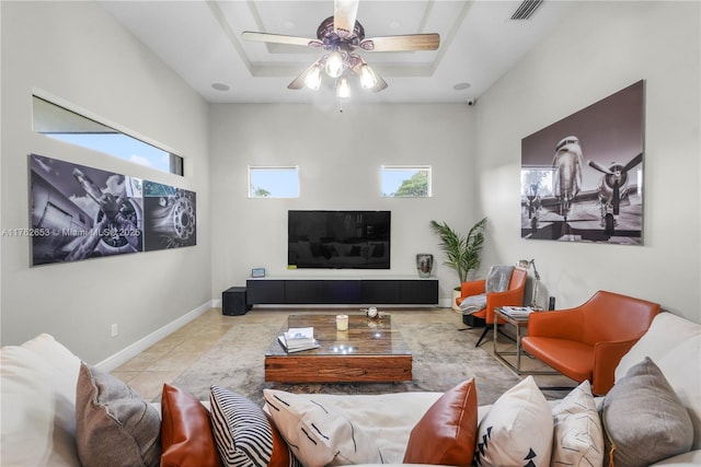 tiled living area with a ceiling fan, a tray ceiling, baseboards, and visible vents