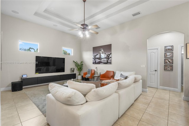 living room with visible vents, a ceiling fan, arched walkways, light tile patterned flooring, and a raised ceiling