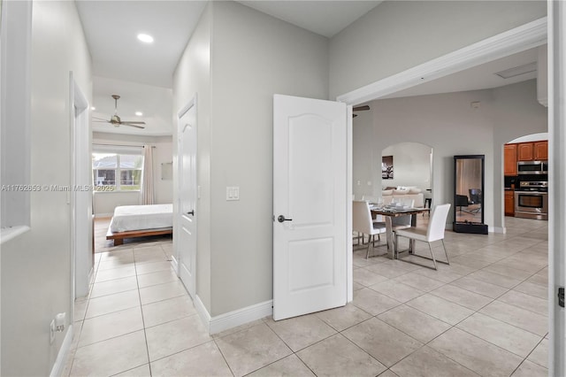 corridor with light tile patterned floors, baseboards, arched walkways, and recessed lighting