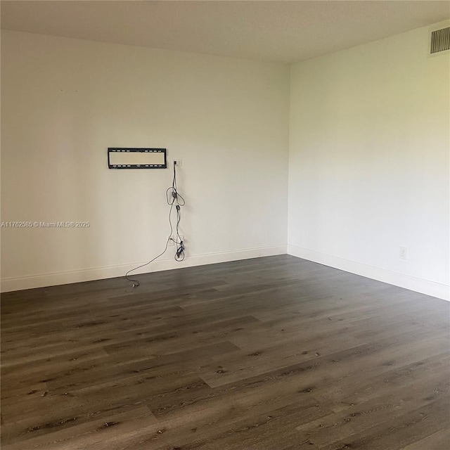 empty room featuring dark wood finished floors, visible vents, and baseboards