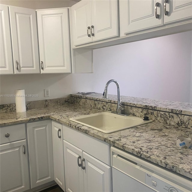 kitchen with white cabinetry, dishwashing machine, light stone countertops, and a sink