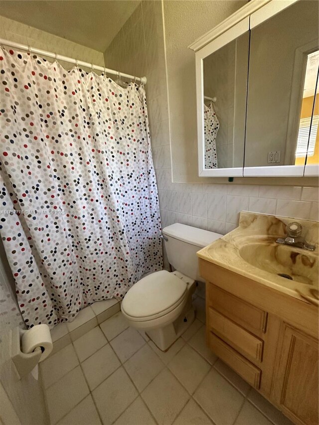 bathroom with tile patterned floors, a shower with curtain, toilet, tile walls, and vanity