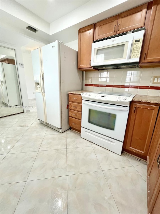 kitchen featuring decorative backsplash, white appliances, visible vents, and brown cabinetry