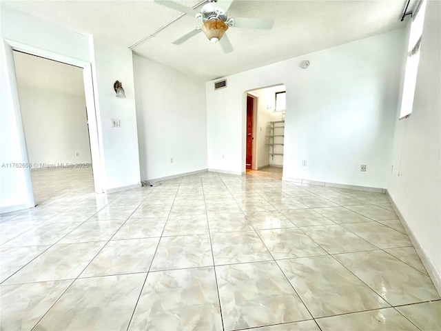 empty room with visible vents, arched walkways, light tile patterned flooring, baseboards, and ceiling fan