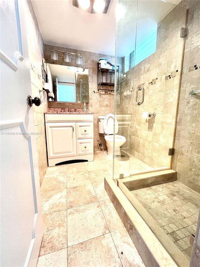 bathroom featuring tile walls, toilet, a shower stall, and vanity