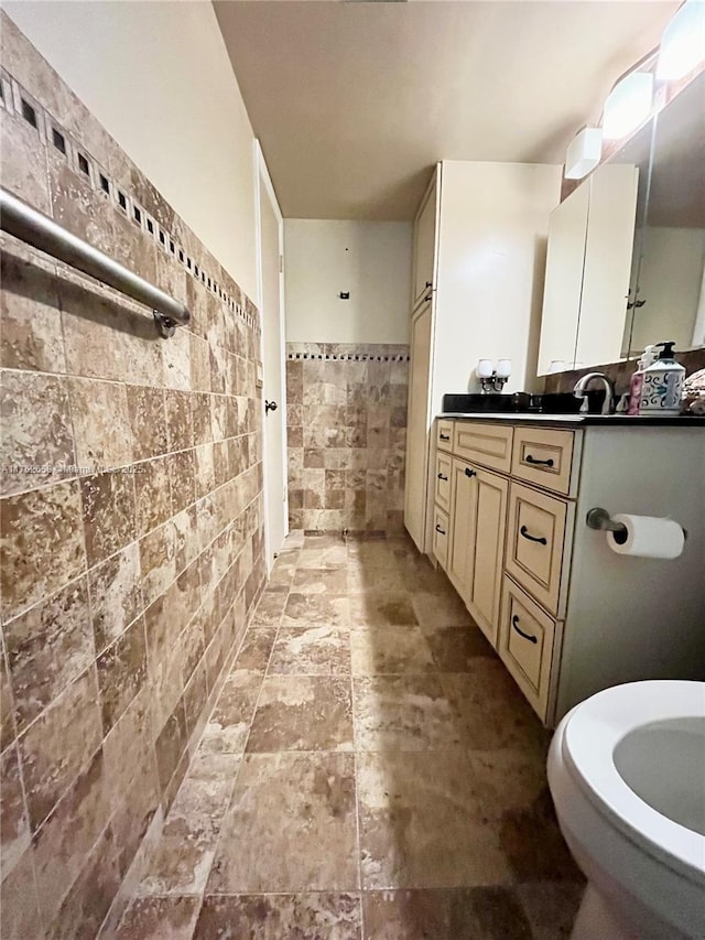 full bath with tile walls, vanity, and stone finish floor