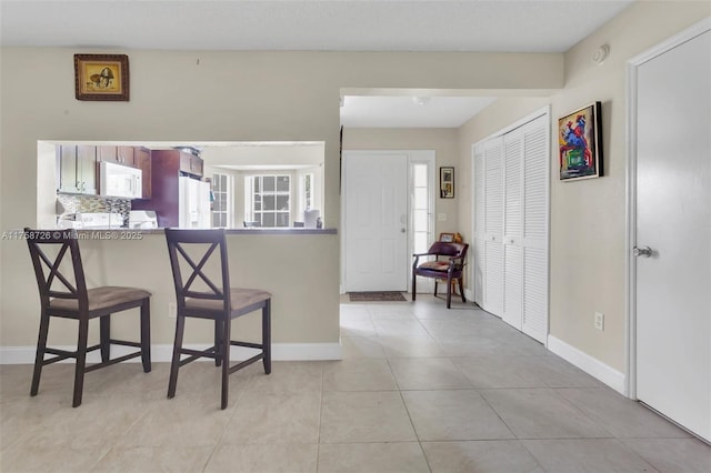 12140 Bruceton Way Unit 102, Orlando, FL 32828 - kitchen featuring light tile patterned floors, baseboards, white appliances, and a breakfast bar area