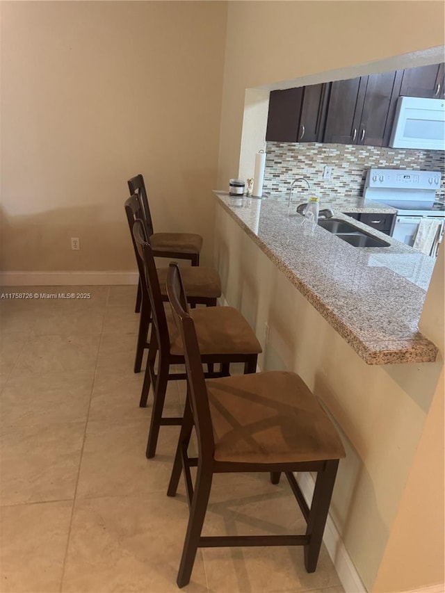 kitchen with backsplash, white appliances, light stone countertops, and a sink