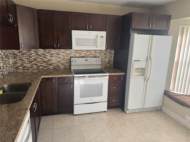 kitchen featuring tasteful backsplash, dark brown cabinets, dark stone countertops, white appliances, and a sink