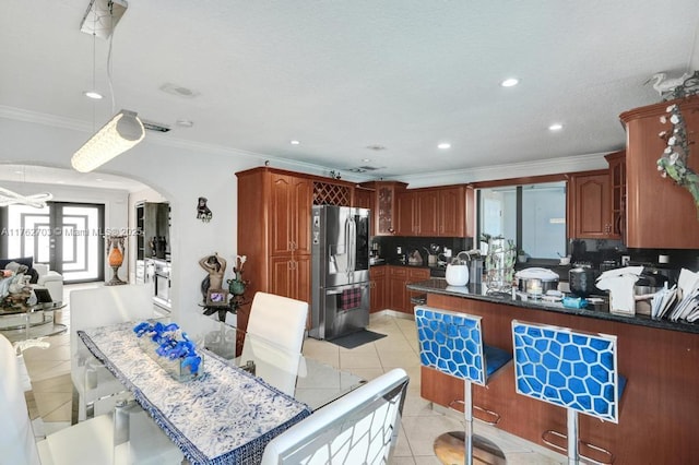 kitchen with stainless steel refrigerator with ice dispenser, tasteful backsplash, arched walkways, crown molding, and light tile patterned floors