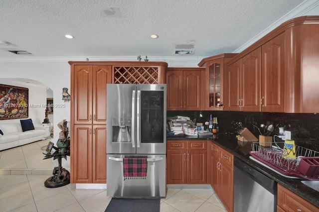 kitchen featuring ornamental molding, arched walkways, appliances with stainless steel finishes, light tile patterned floors, and glass insert cabinets