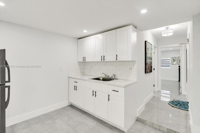 kitchen with tasteful backsplash, baseboards, light countertops, white cabinets, and a sink