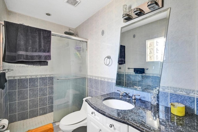 bathroom featuring visible vents, a shower stall, toilet, vanity, and tile walls