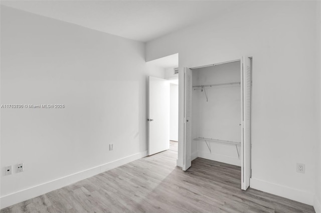 unfurnished bedroom featuring visible vents, wood finished floors, baseboards, and a closet