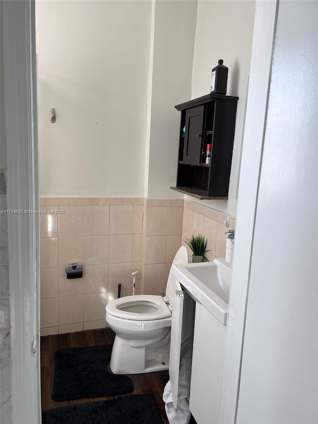 bathroom with a wainscoted wall, toilet, wood finished floors, tile walls, and vanity