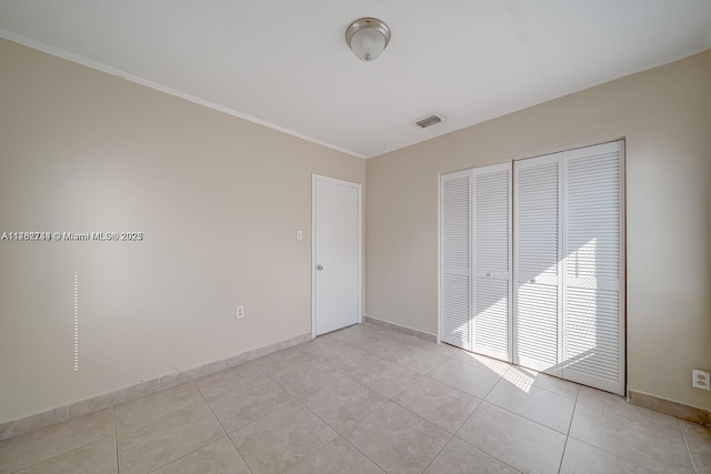 unfurnished bedroom with visible vents, a closet, light tile patterned flooring, crown molding, and baseboards