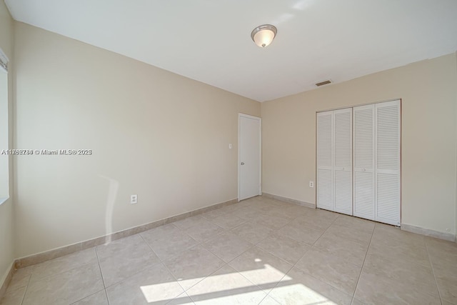 unfurnished bedroom featuring a closet, visible vents, baseboards, and light tile patterned floors