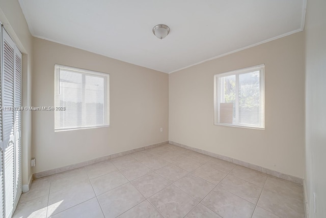 empty room featuring light tile patterned floors, baseboards, and ornamental molding