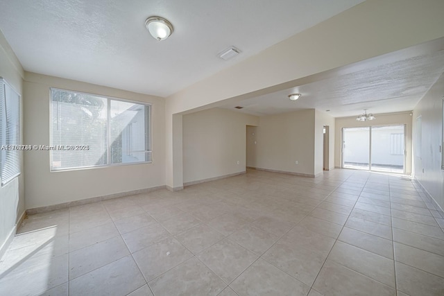 unfurnished room featuring light tile patterned floors, a chandelier, a textured ceiling, and baseboards