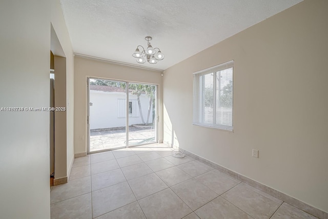 spare room with an inviting chandelier, light tile patterned floors, baseboards, and a textured ceiling