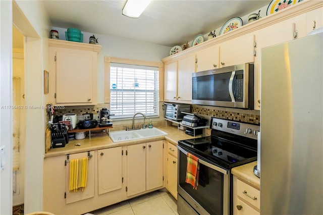 kitchen with a sink, tasteful backsplash, stainless steel appliances, light tile patterned flooring, and light countertops