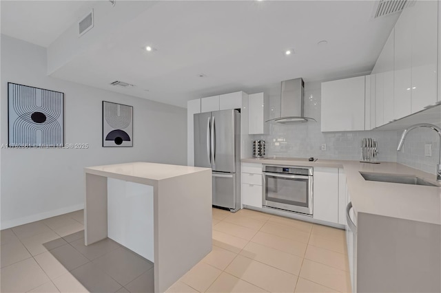 kitchen featuring a kitchen island, wall chimney range hood, appliances with stainless steel finishes, modern cabinets, and a sink