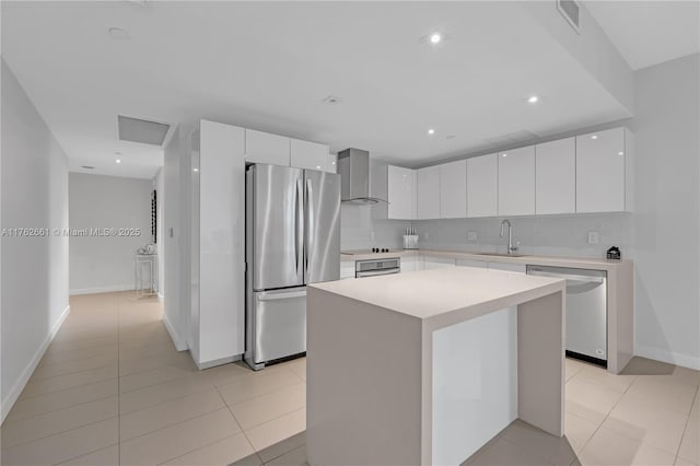 kitchen with a sink, backsplash, appliances with stainless steel finishes, white cabinets, and wall chimney range hood