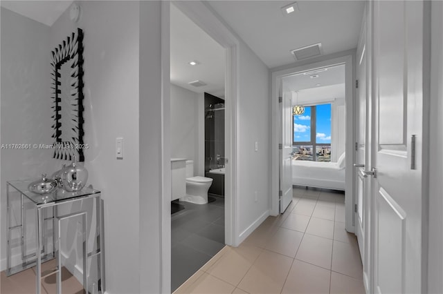 hall featuring light tile patterned floors, visible vents, and baseboards