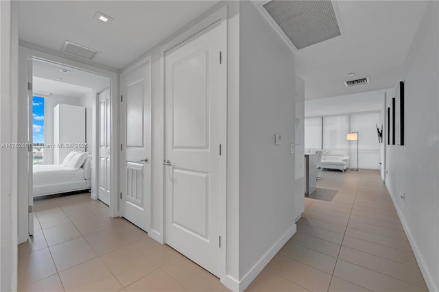 hallway with attic access, light tile patterned floors, and visible vents