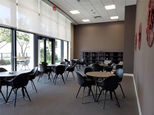 dining area with visible vents, carpet, baseboards, a high ceiling, and a paneled ceiling