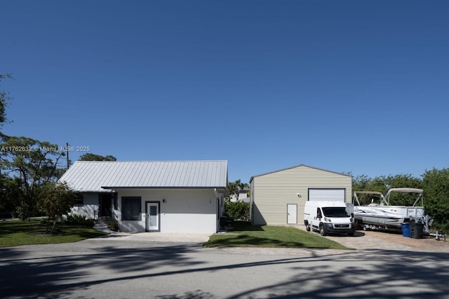 view of front of house with a front lawn, metal roof, a garage, an outdoor structure, and driveway