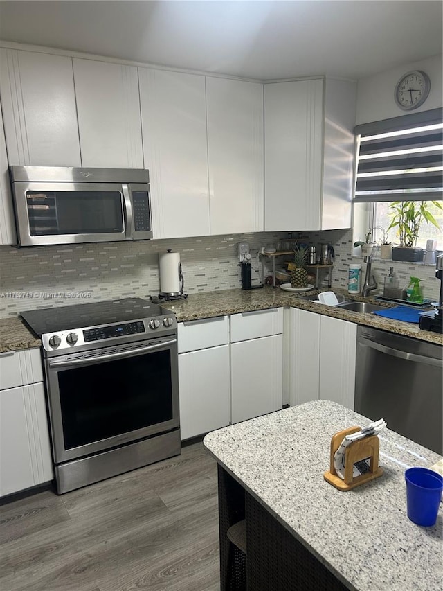 kitchen featuring white cabinetry, wood finished floors, tasteful backsplash, and stainless steel appliances