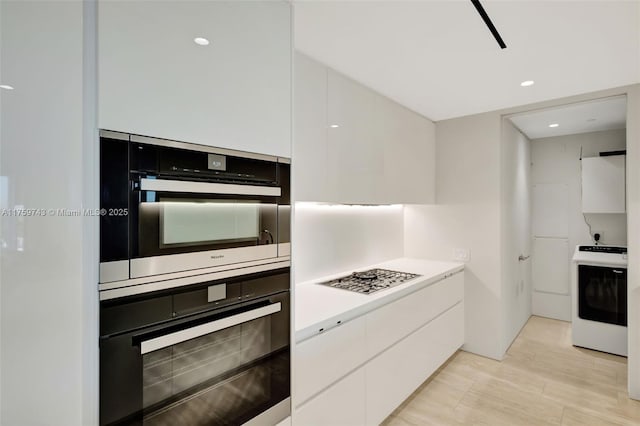 kitchen featuring washer / dryer, gas stovetop, light countertops, white cabinetry, and modern cabinets