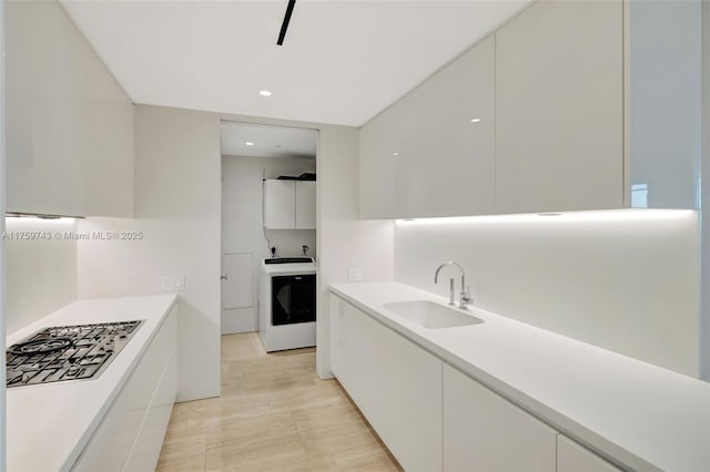 kitchen with a sink, washer / clothes dryer, modern cabinets, and white cabinetry