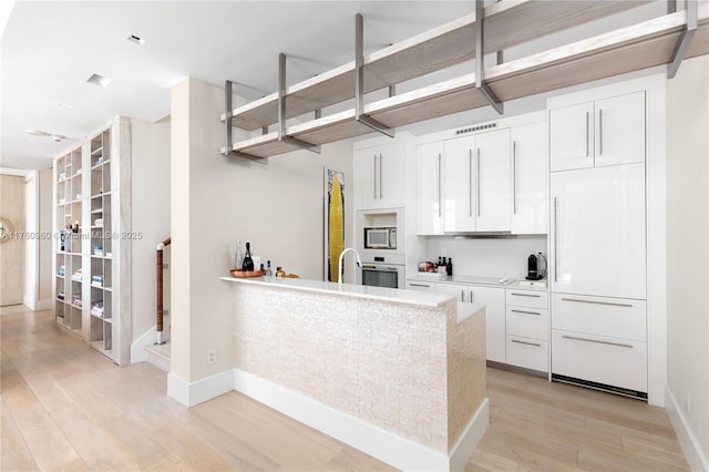 kitchen with stainless steel microwave, visible vents, light countertops, light wood-style flooring, and white oven