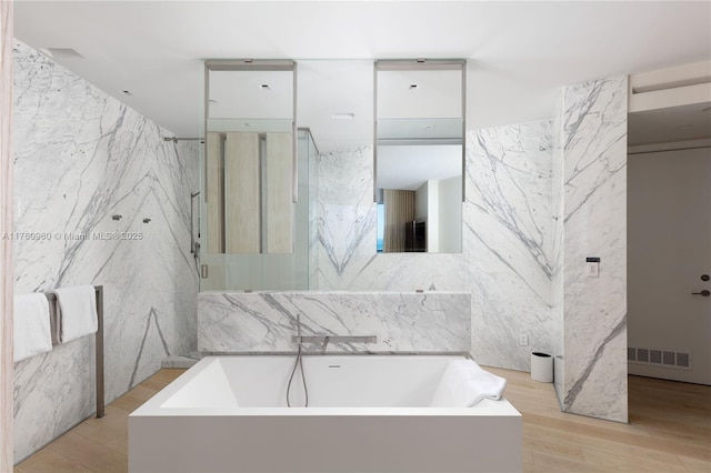 bathroom featuring a marble finish shower, visible vents, a bathing tub, wood finished floors, and tile walls